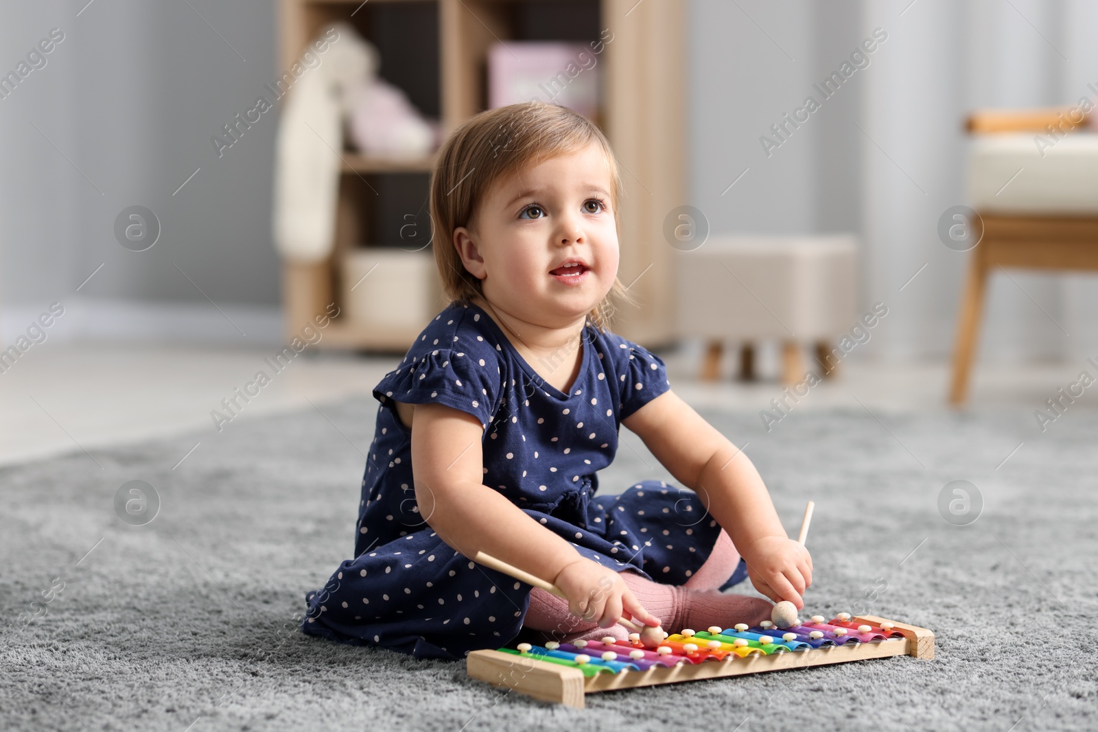 Photo of Cute little girl playing with toy xylophone on floor at home