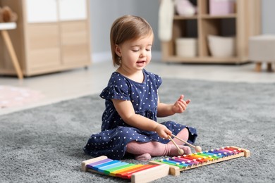 Photo of Cute little girl playing with toy xylophones on floor at home