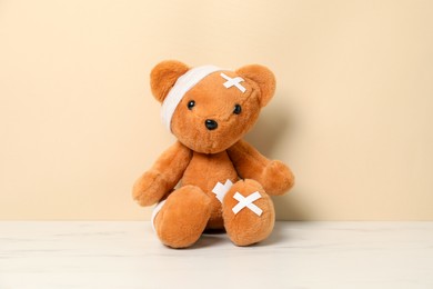 Photo of Teddy bear with bandages and sticking plasters on white marble table against beige background