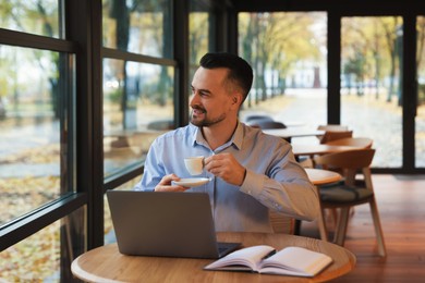 Photo of Man with cup of coffee working at table in cafe