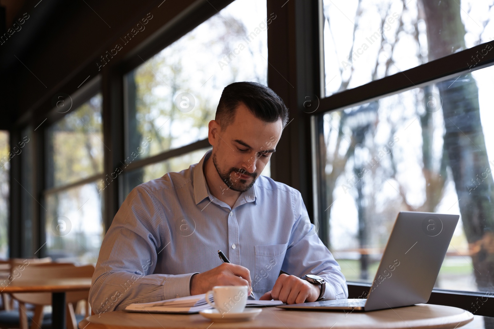 Photo of Man taking notes at table in cafe