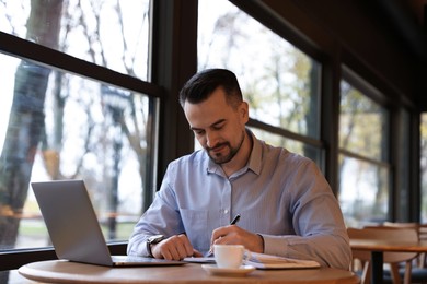 Photo of Man taking notes at table in cafe