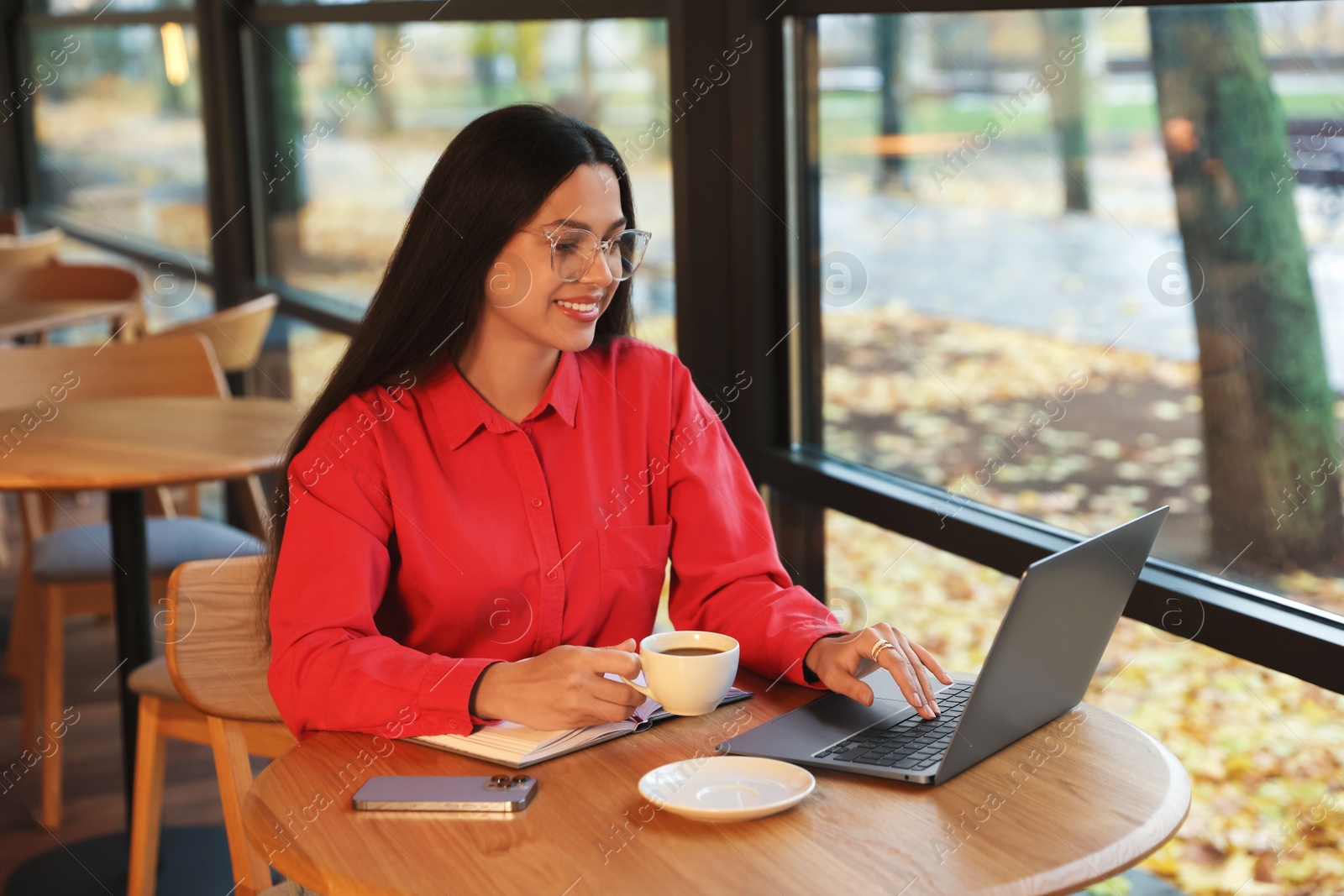 Photo of Woman with cup of coffee working on laptop at table in cafe