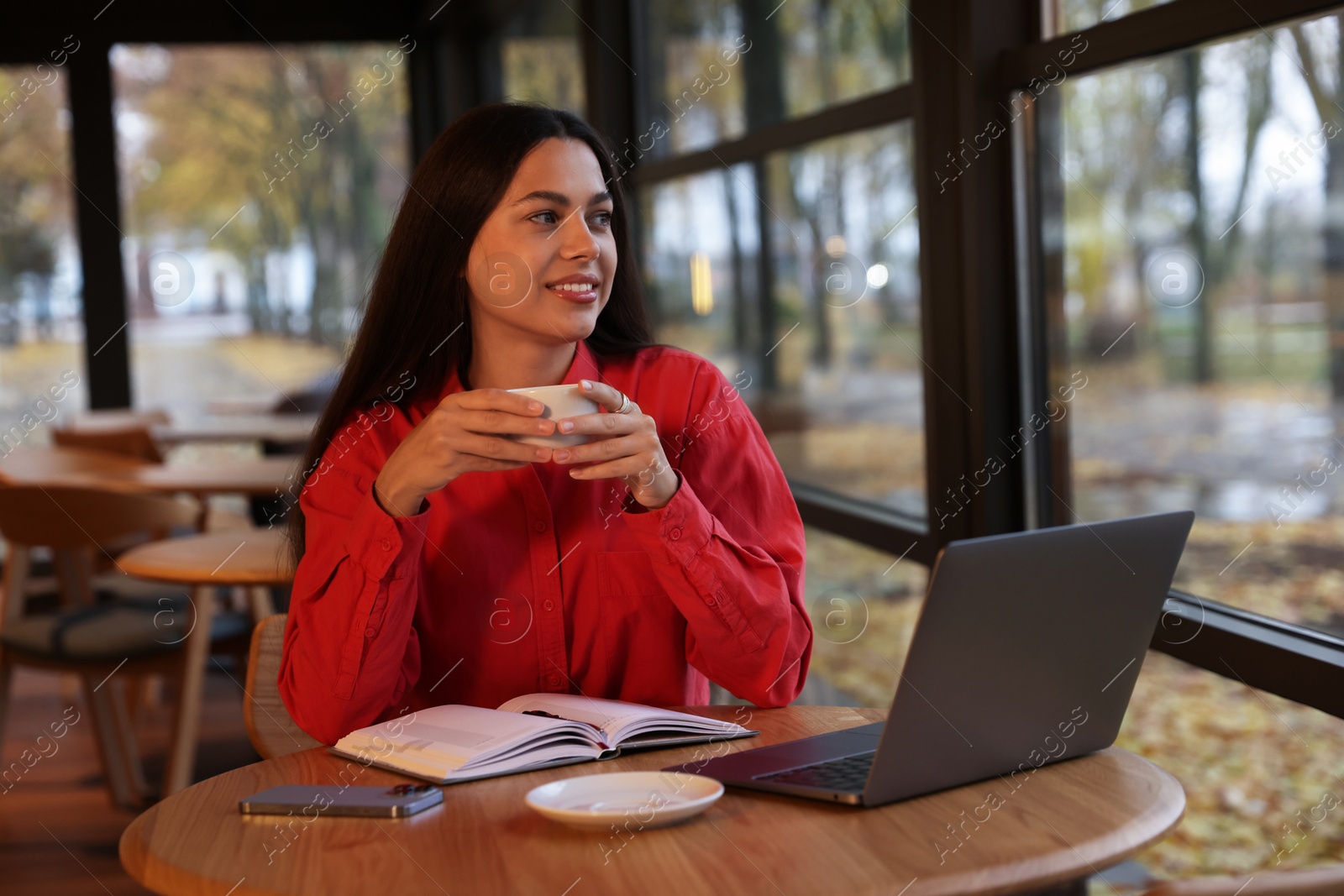 Photo of Woman with cup of coffee working at table in cafe