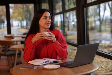 Photo of Woman with cup of coffee working at table in cafe