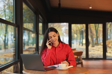 Photo of Woman talking on smartphone while working at table in cafe