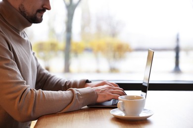 Photo of Man working on laptop at wooden table in cafe, closeup