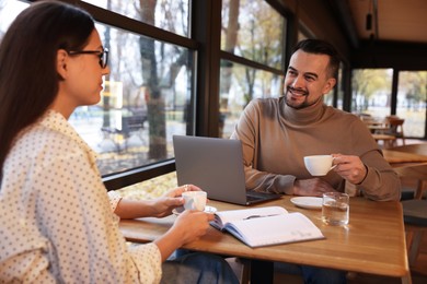 Photo of Colleagues with cups of coffee working together at table in cafe