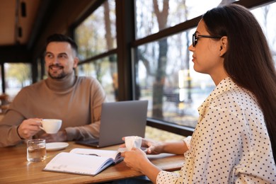 Photo of Colleagues with cups of coffee working together at table in cafe