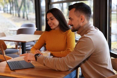 Photo of Colleagues with laptop working together at table in cafe