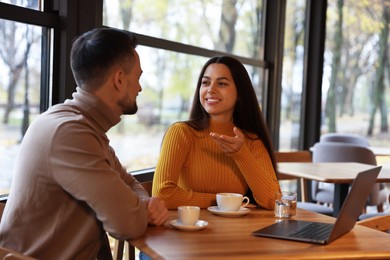 Photo of Colleagues with laptop working together at table in cafe