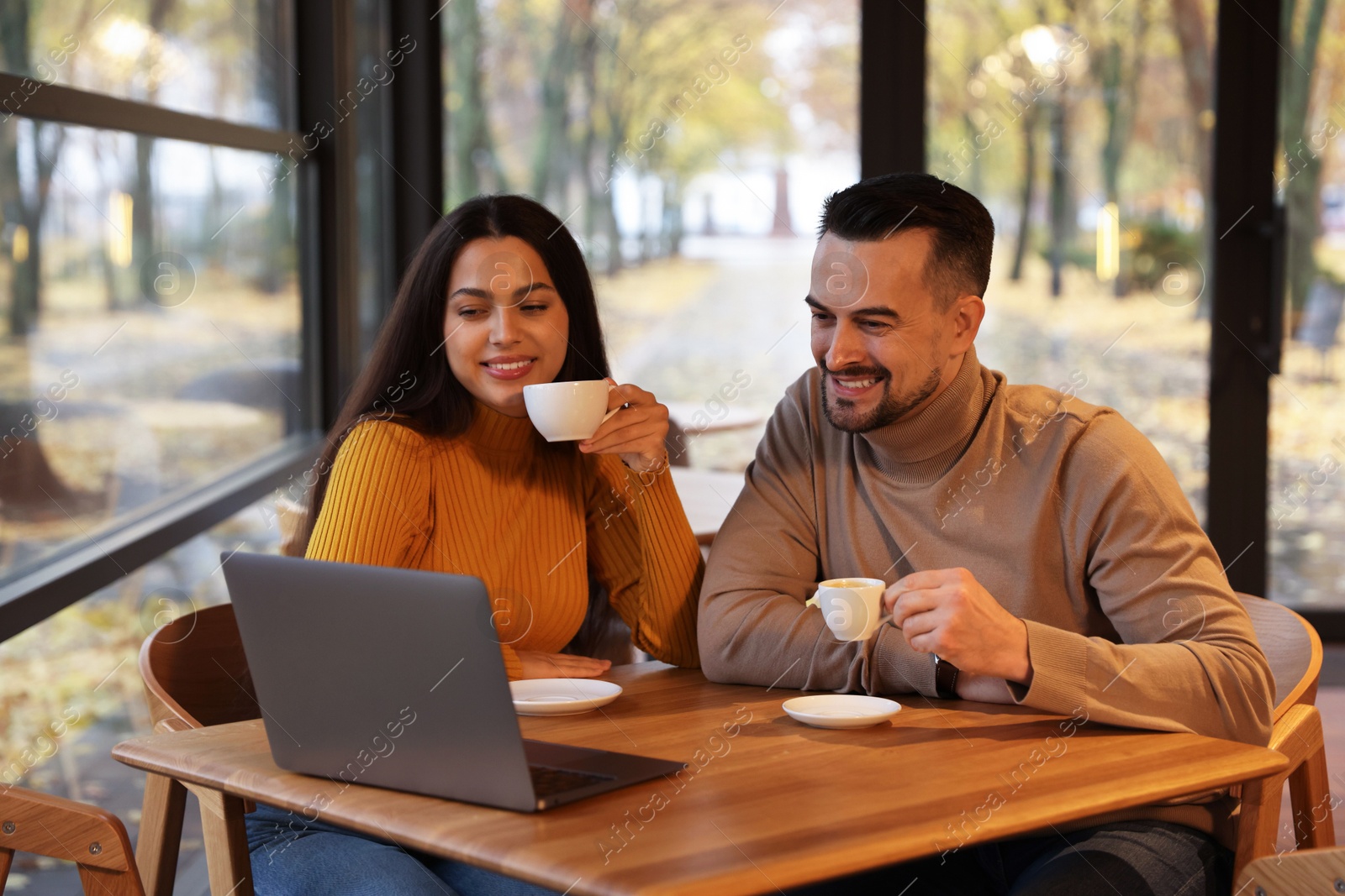 Photo of Colleagues with cups of coffee and laptop working together at table in cafe