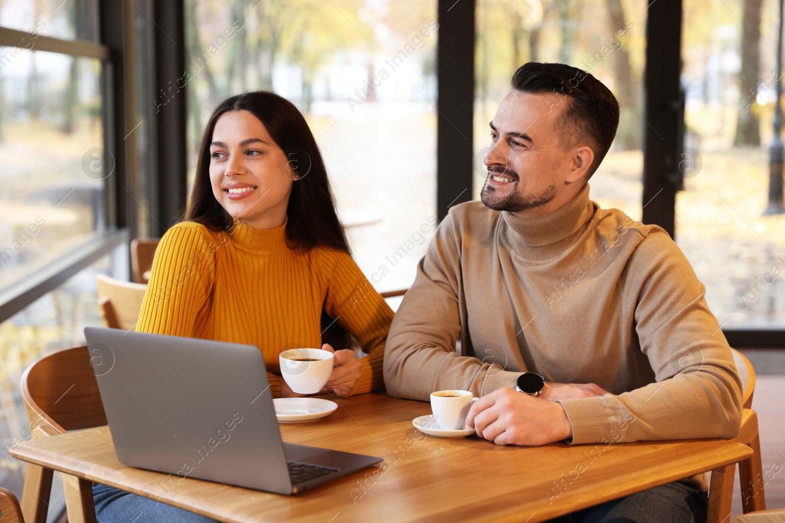 Photo of Colleagues with cups of coffee and laptop working together at table in cafe