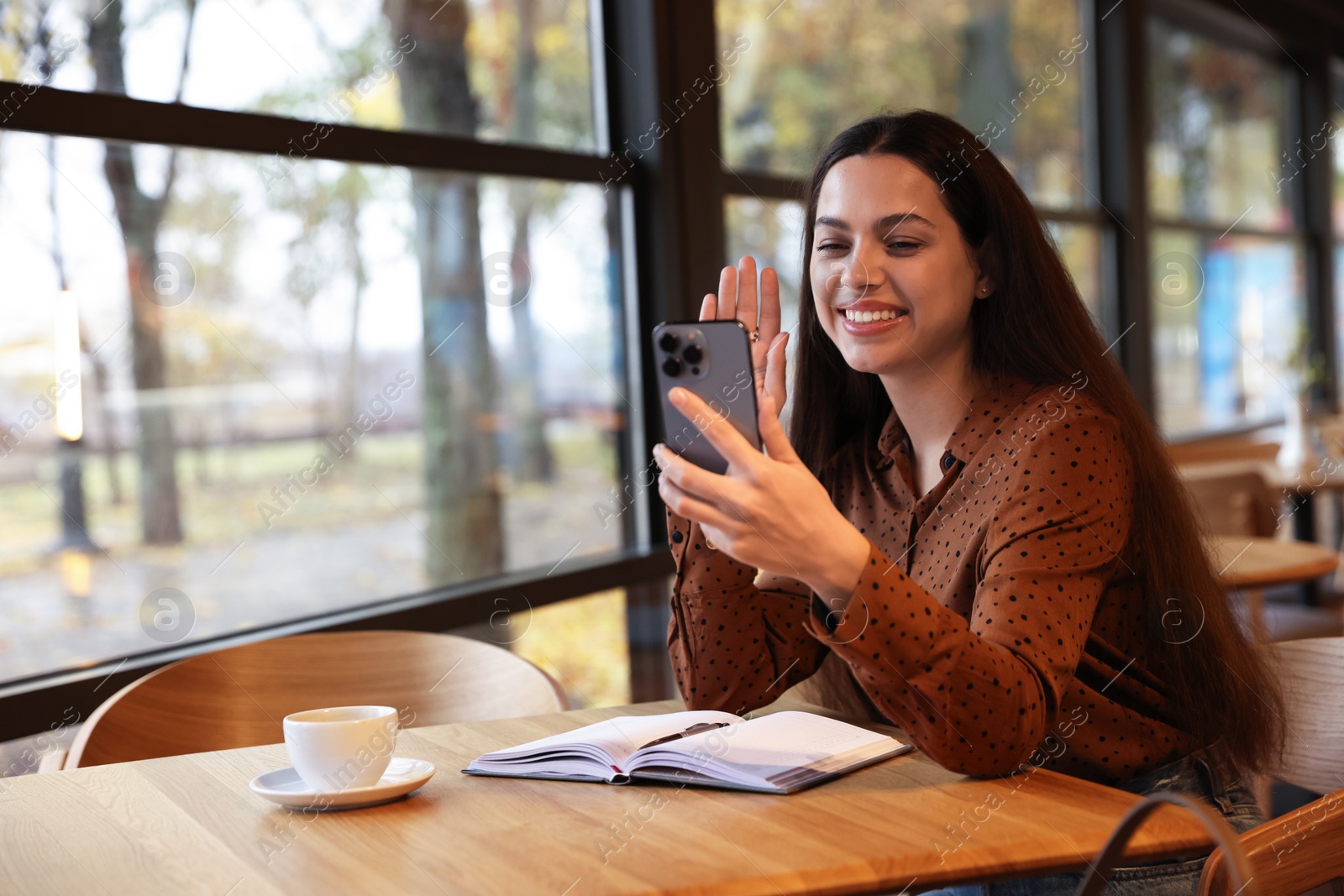 Photo of Woman having video chat via smartphone at table in cafe, space for text