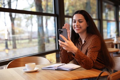 Photo of Woman having video chat via smartphone at table in cafe, space for text