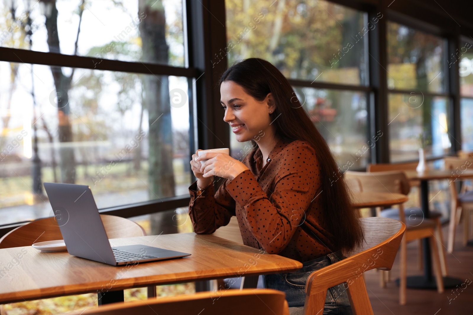 Photo of Woman with cup of coffee working at table in cafe