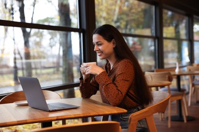 Photo of Woman with cup of coffee working at table in cafe