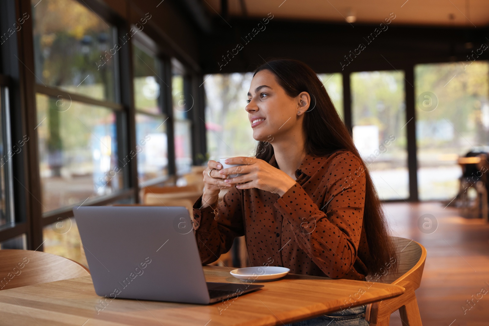 Photo of Woman with cup of coffee working at table in cafe