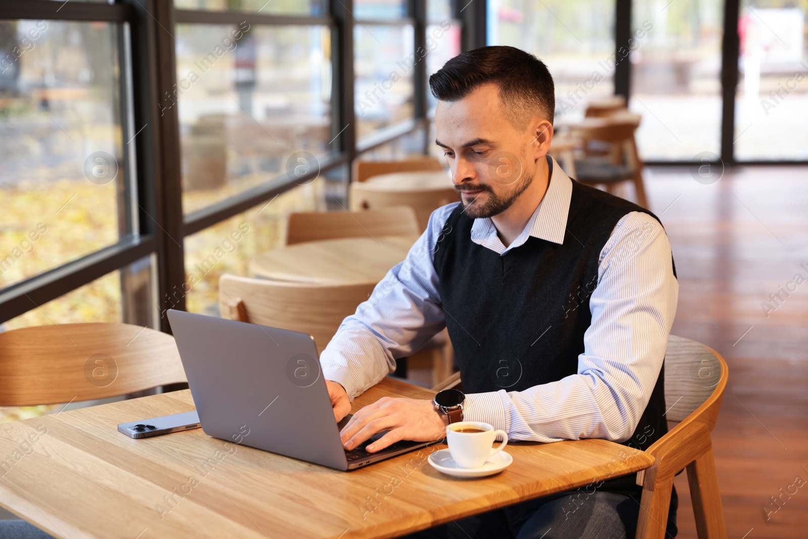 Photo of Man working on laptop at table in cafe