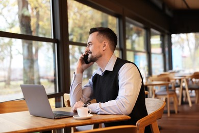 Photo of Man talking on smartphone while working at table in cafe