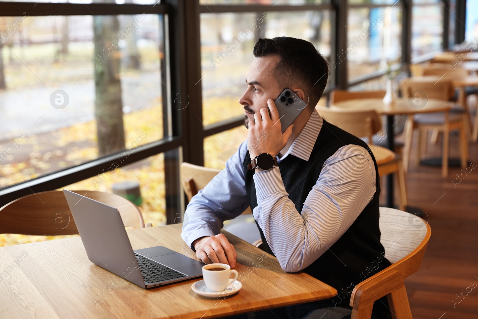 Photo of Man talking on smartphone while working at table in cafe