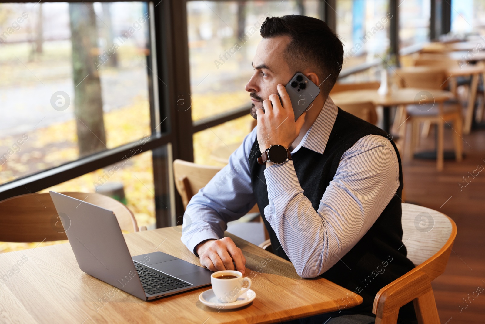 Photo of Man talking on smartphone while working at table in cafe