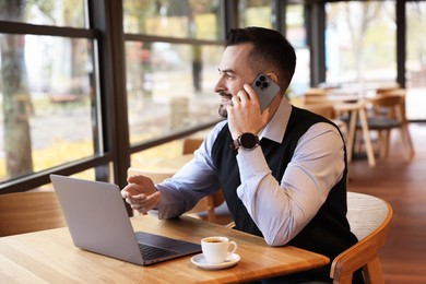 Photo of Man talking on smartphone while working at table in cafe