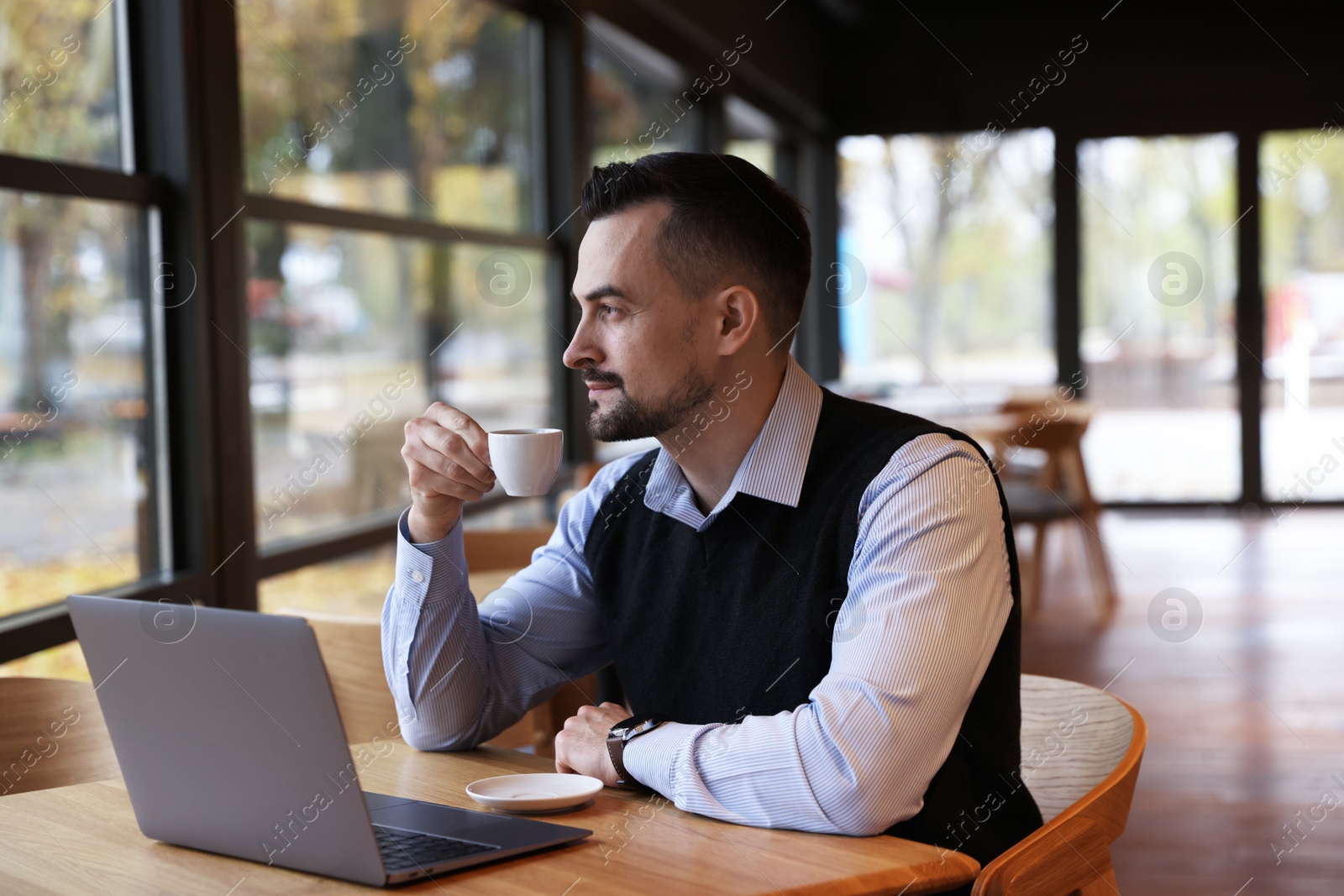 Photo of Man with cup of coffee working at table in cafe