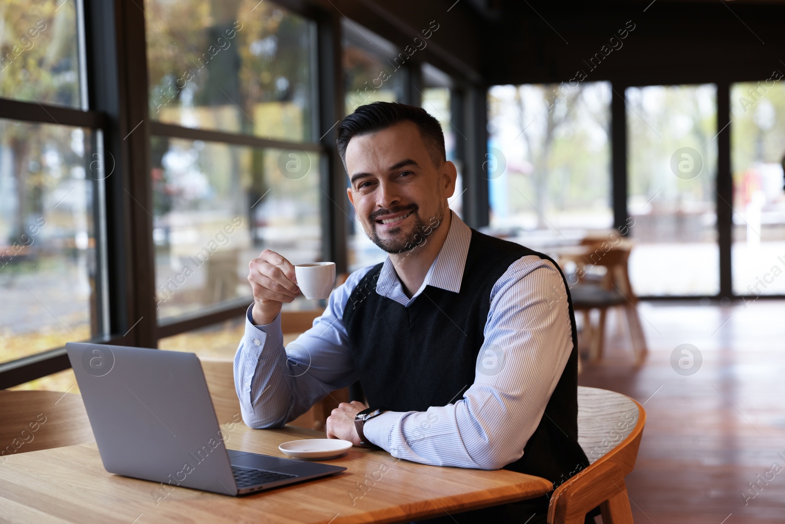 Photo of Man with cup of coffee working at table in cafe