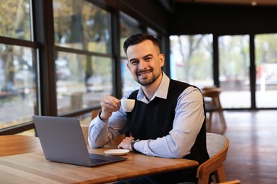 Photo of Man with cup of coffee working at table in cafe