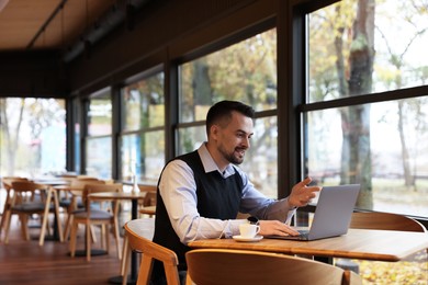 Man having video chat via laptop at table in cafe, space for text