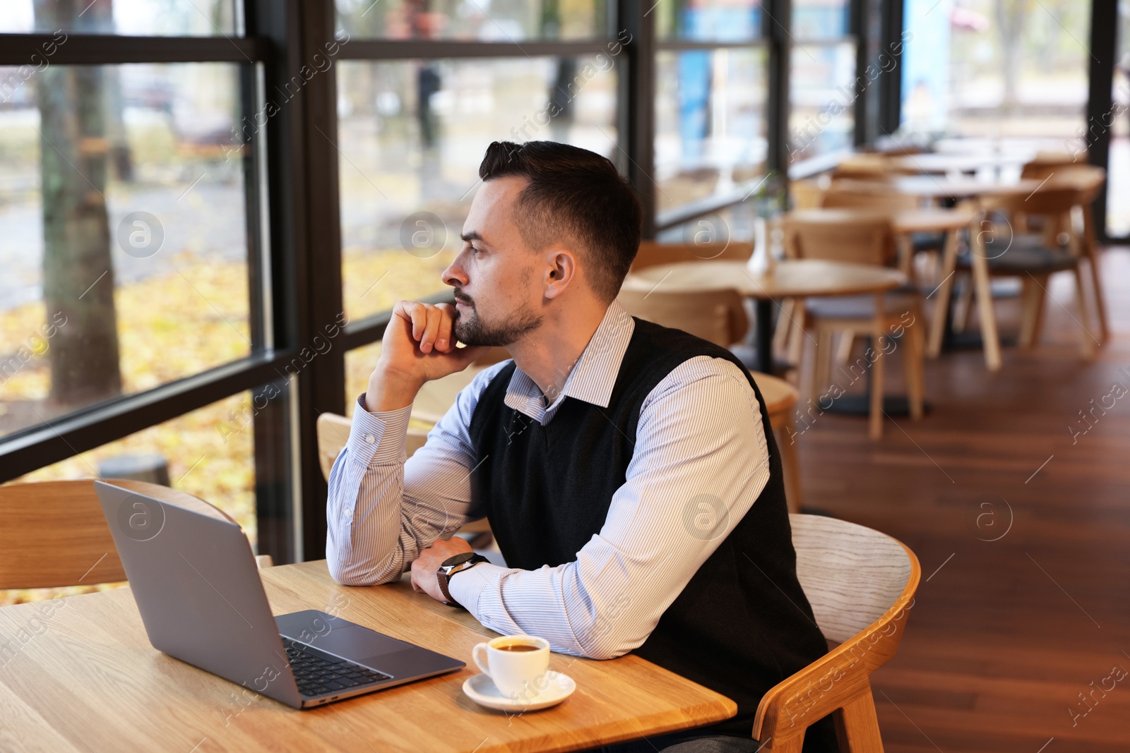 Photo of Man with laptop and cup of coffee at table in cafe