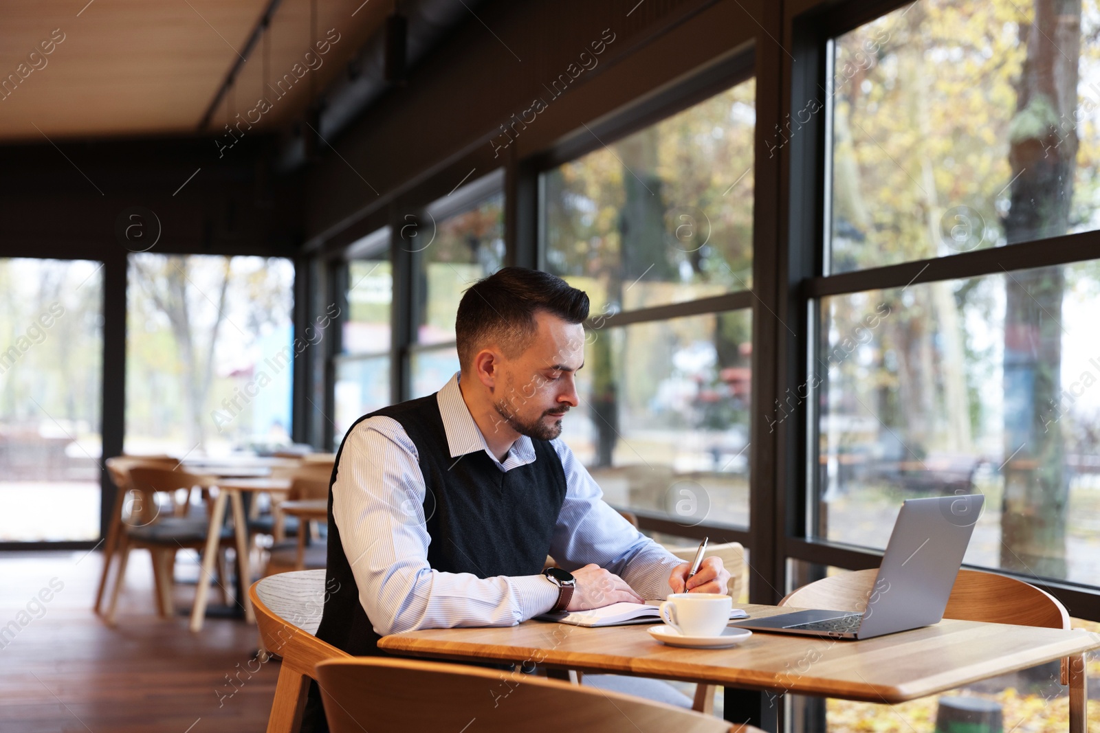 Photo of Man taking notes at table in cafe