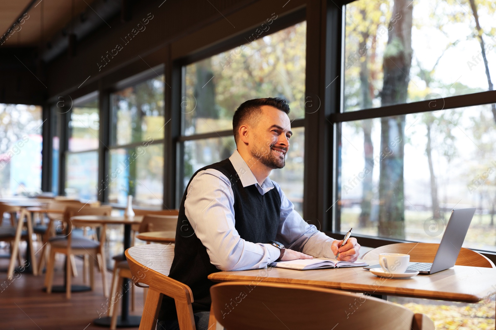 Photo of Man taking notes at table in cafe