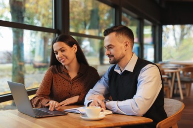 Photo of Colleagues with laptop working together in cafe