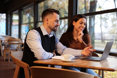 Photo of Colleagues with laptop working together in cafe