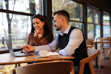 Photo of Colleagues with laptop working together in cafe