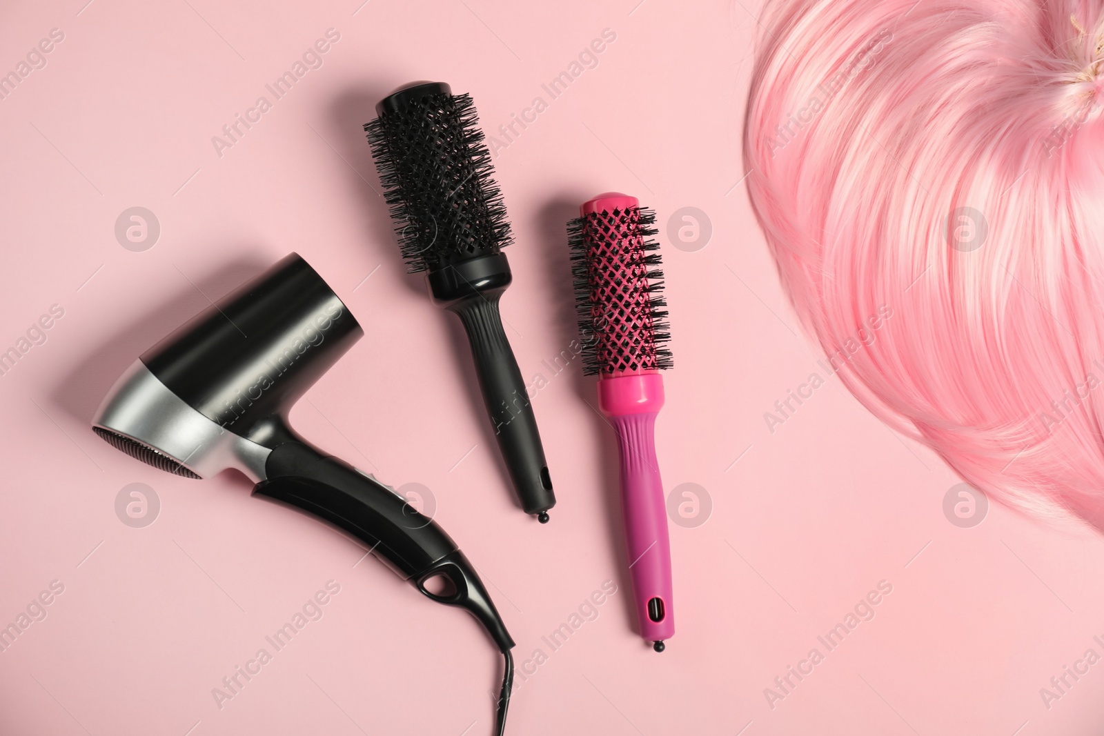 Photo of Stylish round brushes, hairdryer and lock of dyed hair on pink background, flat lay