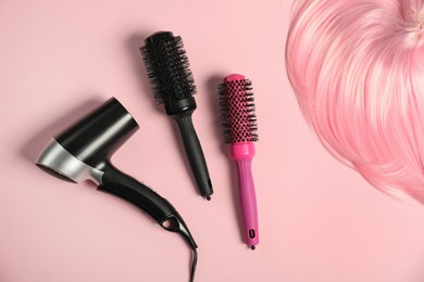 Photo of Stylish round brushes, hairdryer and lock of dyed hair on pink background, flat lay