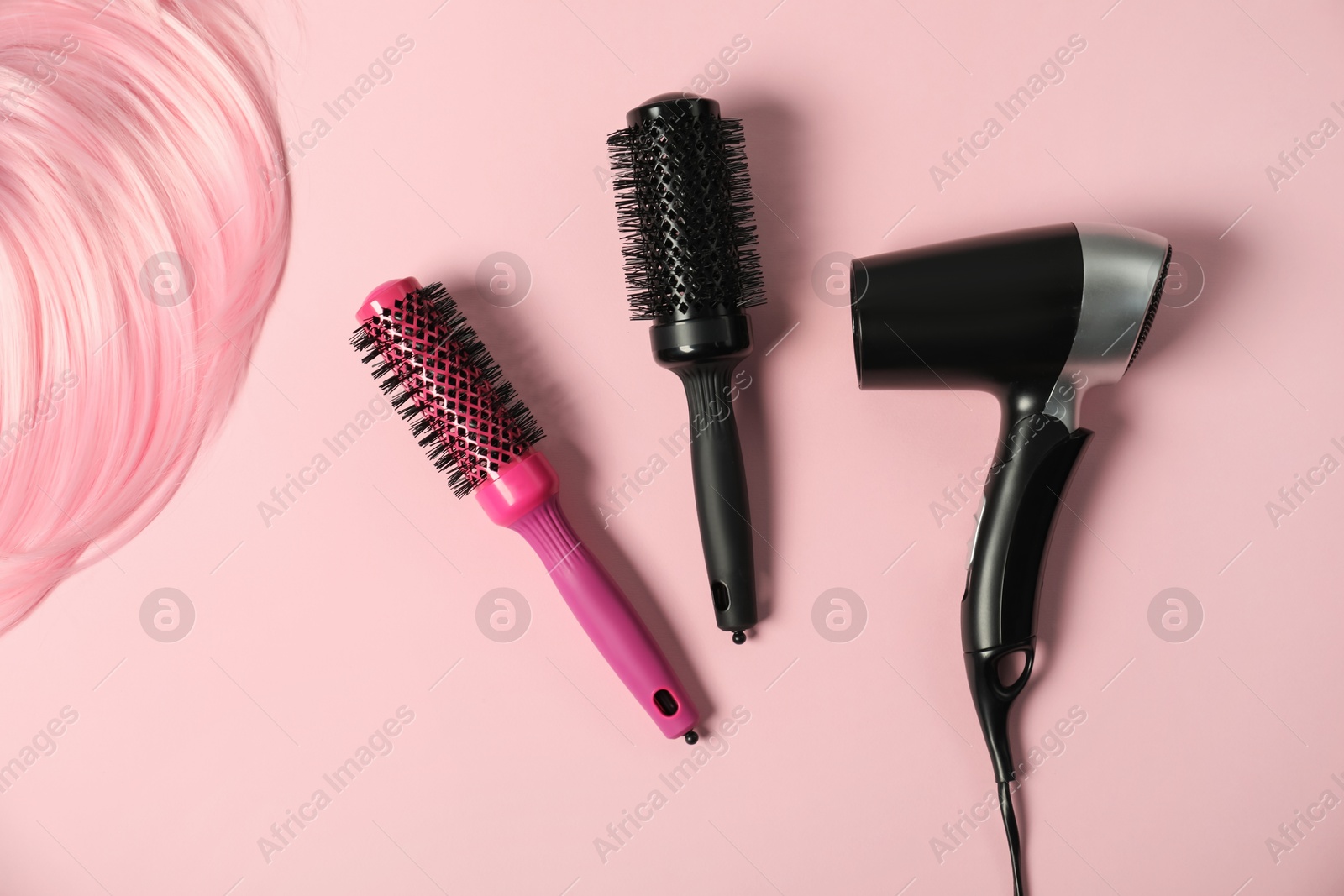 Photo of Stylish round brushes, hairdryer and lock of dyed hair on pink background, flat lay