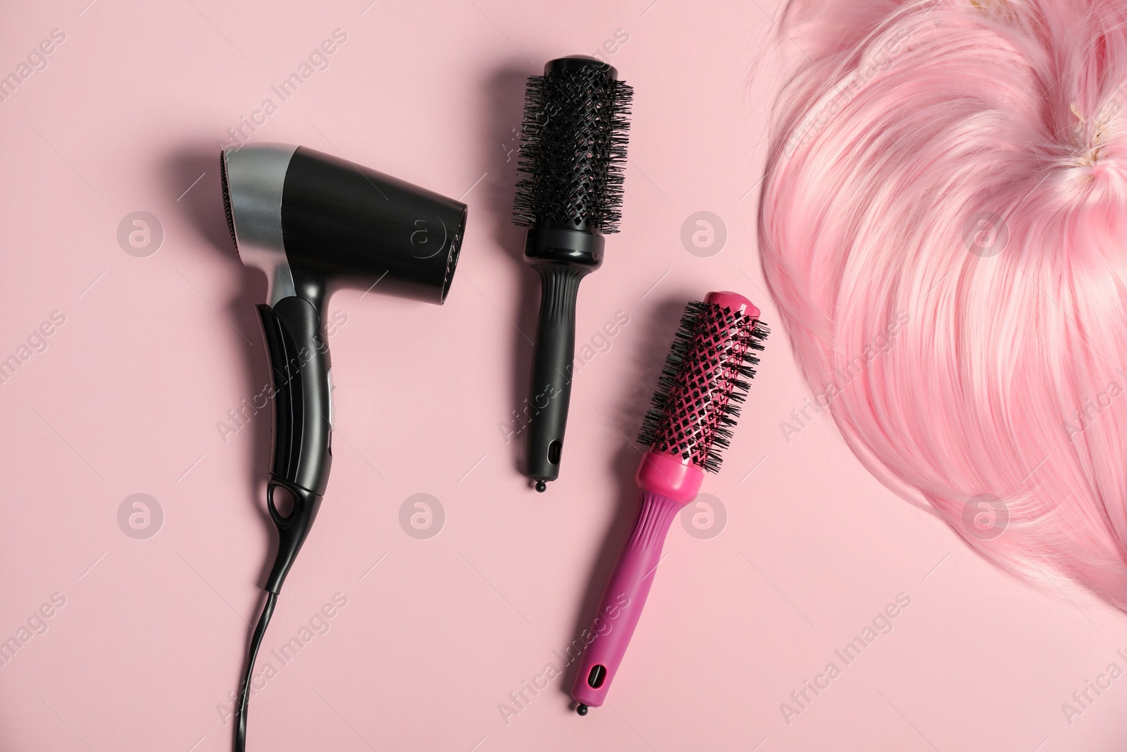 Photo of Stylish round brushes, hairdryer and lock of dyed hair on pink background, flat lay