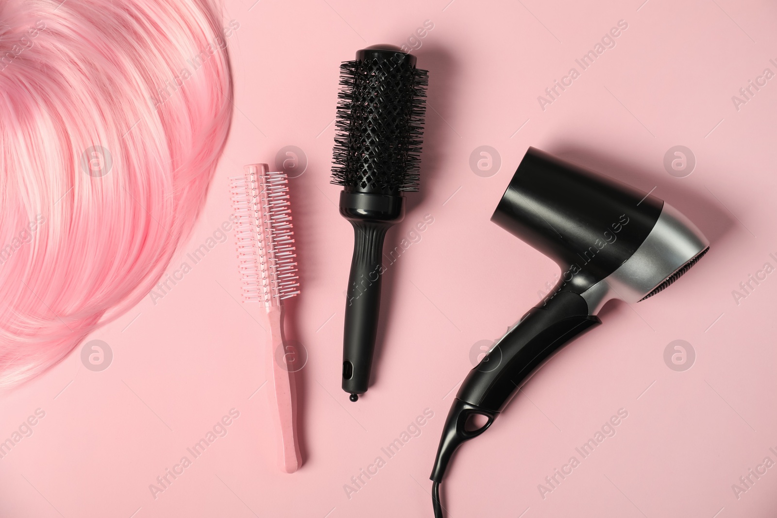 Photo of Stylish round brushes, hairdryer and lock of dyed hair on pink background, flat lay