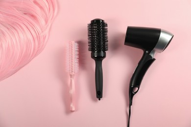 Photo of Stylish round brushes, hairdryer and lock of dyed hair on pink background, flat lay