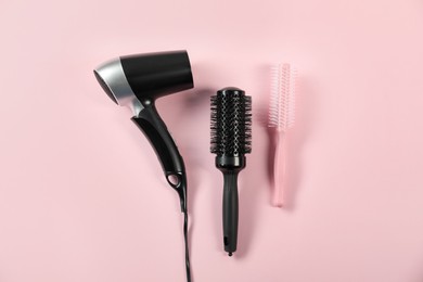 Photo of Stylish round brushes and hairdryer on pink background, flat lay