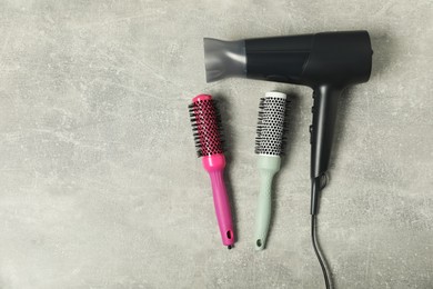 Photo of Stylish round brushes and hairdryer on light grey table, flat lay. Space for text