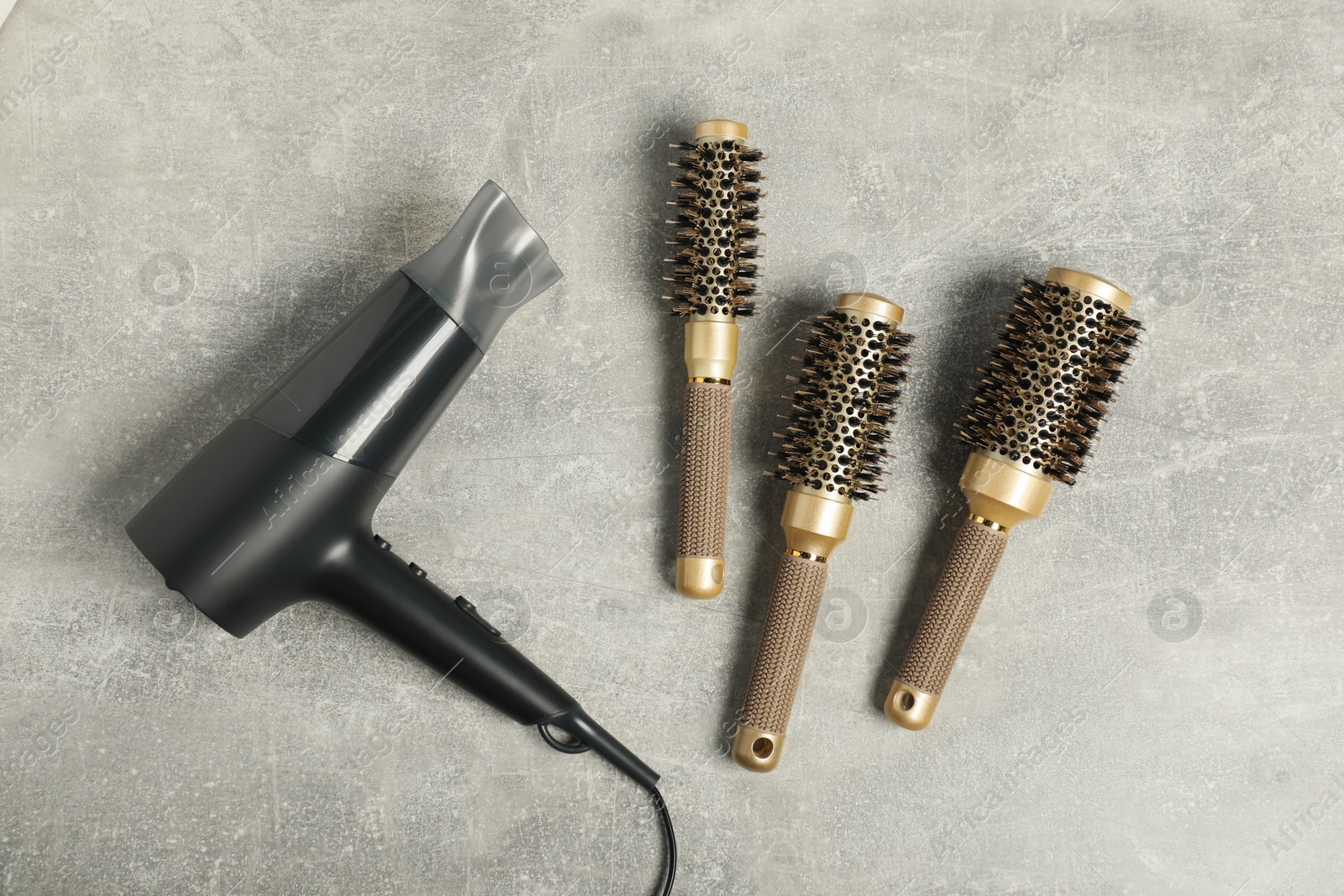 Photo of Stylish round brushes and hairdryer on light grey table, flat lay