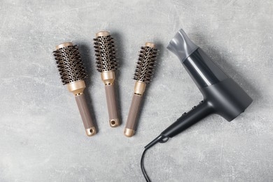 Photo of Stylish round brushes and hairdryer on light grey table, flat lay