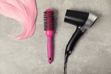 Photo of Stylish round brush, lock of pink hair and hairdryer on light grey table, flat lay