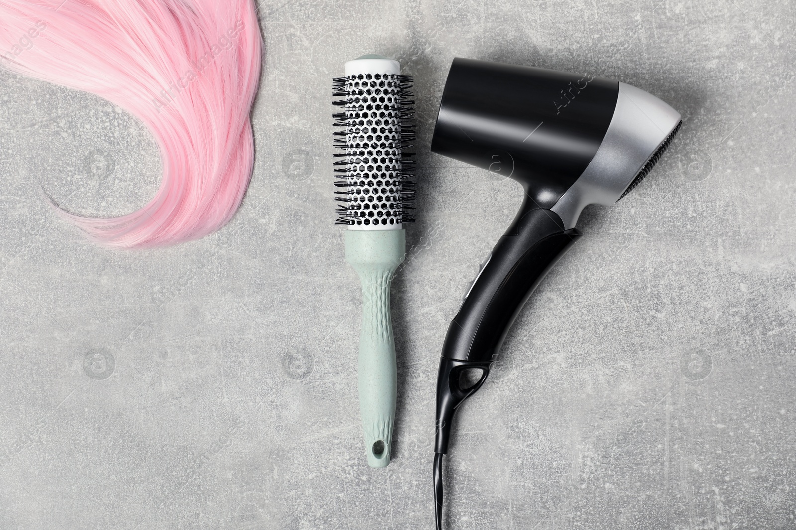 Photo of Stylish round brush, lock of pink hair and hairdryer on light grey table, flat lay