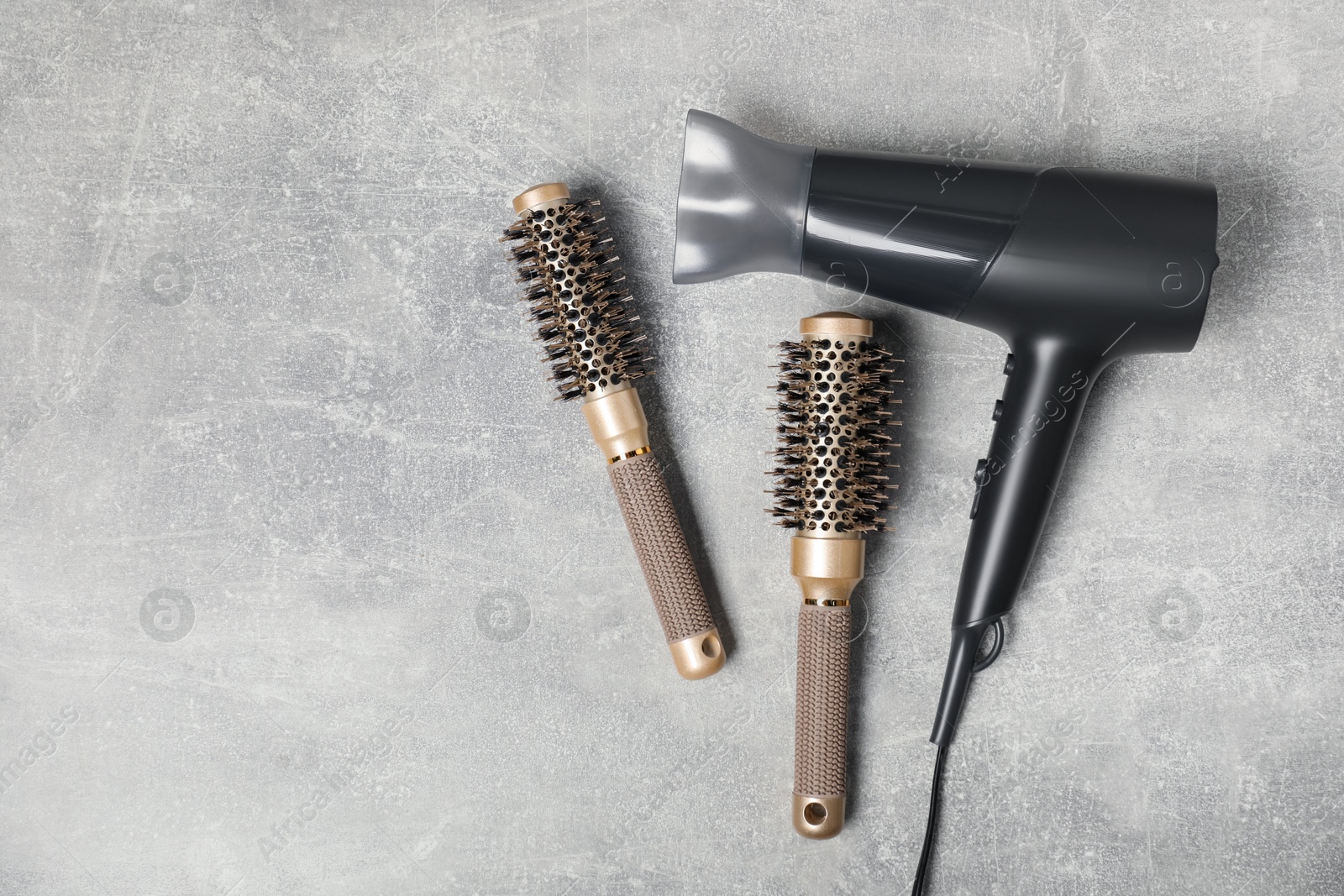 Photo of Stylish round brushes and hairdryer on light grey table, flat lay. Space for text